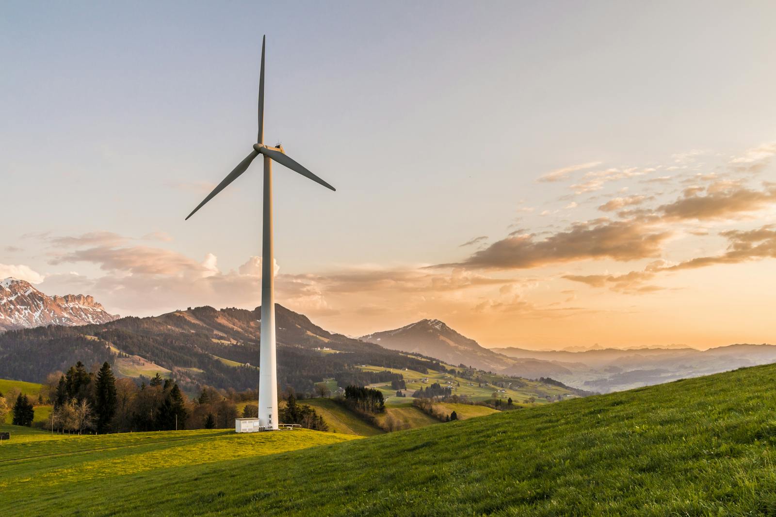 Éolienne au milieu de collines et de montagnes au coucher du soleil, symbolisant l'énergie renouvelable et le développement durable.